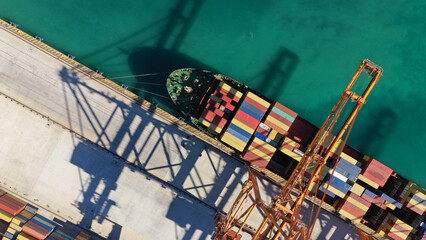 Aerial top down photo of cranes loading - unloading container ship anchored in logistics terminal...