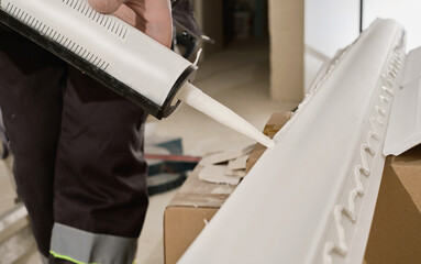 Master applies glue to the baseboard with a glue gun, hands close-up. The process of installing a...