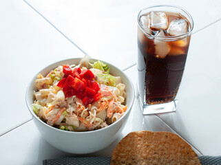 Tuna salad in a white bowl with lettuce pasta carrots and red peppers on top with a dark soft drink and a tostada on the side. Horizontal