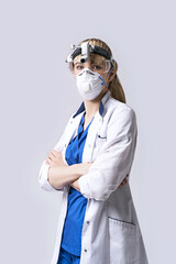 Confident ENT doctor wearing surgical headlight head lantern, protective face mask and glasses. Portrait of female otolaryngologist standing arms crossed on light grey background.