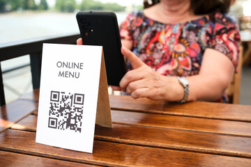 Mature unrecognizable woman scanning a QR code to access an online restaurant menu. Concept of...