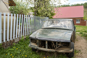 Rusty, broken car near the fence near the house