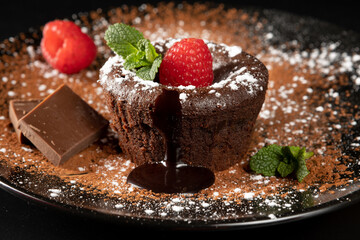 Small chocolate cake filled with liquid chocolate. Traditional French dessert coulant. Tasty hot cake melting chocolate syrup and decorated with cocoa powder, icing sugar, raspberries and mint. Meltin