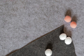 Colored white and soft pink soft felt / wool balls on a gray felt background.