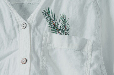 Close up of a organic linen white shirt with coconut buttons, with fir branch in the chest pocket