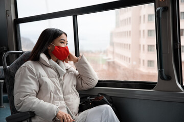 Thoughtful Asian woman in mask looking out bus window