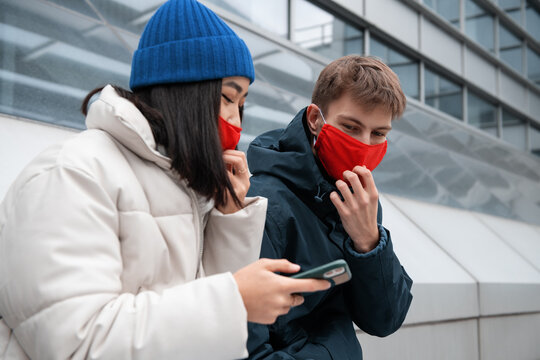 Diverse couple in masks using smartphone on street