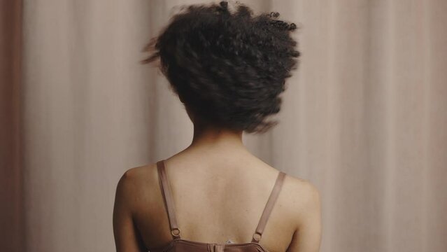 Back view of young curly african american woman touching hair and shaking head, enjoying hairstyle, smiling to camera