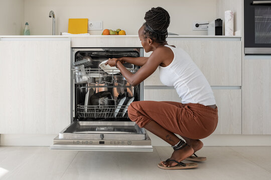 Black housewife putting dishware in dishwasher