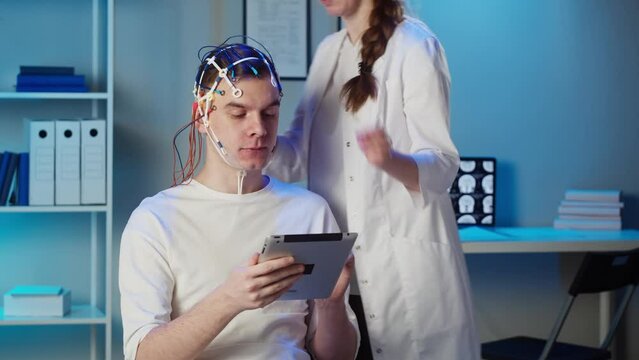 EEG topographer for examining brain, doctor making electrogram of scalp activity. Researching of brain work, man using gadget wearing electroencephalography headset.