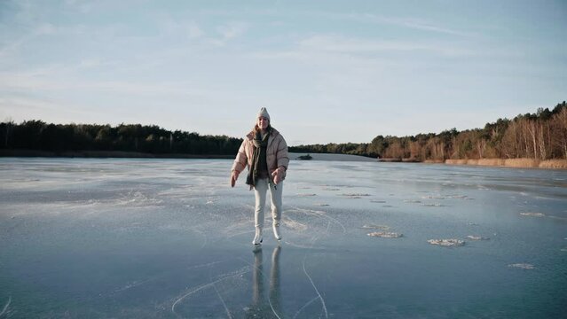 Woman ice skating on a frozen lake on a sunny winter day approaching the camera. Sunny ice skating day in beautiful landscape. Girl in white skates on blue lake. High quality 4k footage