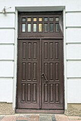 one old brown door made of wood and glass on a white concrete wall of a historical building on the street