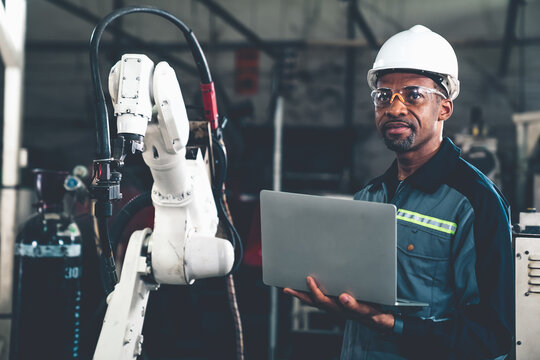 African American factory worker working with adept robotic arm in a workshop . Industry robot programming software for automated manufacturing technology .