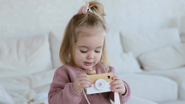 Small adorable girl playing with wooden toy camera 