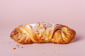 croissant sprinkled with almonds on a pink background, close-up