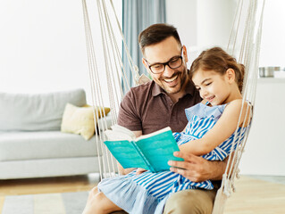 child daughter family happy reading book education literature father sofa playing fun together girl...