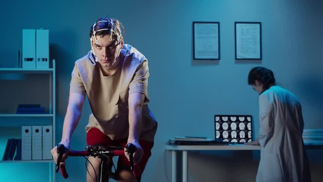 EEG topographer for examining brain, doctor making electrogram of scalp activity. Researching of brain work, man riding bicycle in electroencephalography headset. Rehabilitation after damage in sport.