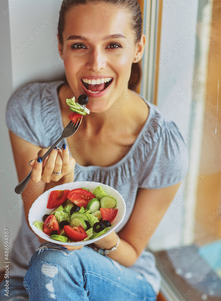 Wall mural a beautiful girl eating healthy food, sitting near window