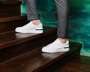 A man in leather white sneakers walks the steps.