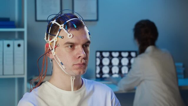 Man wearing EEG topographer for examining brain, doctor making electrogram of scalp activity. Researching of brain work using electroencephalography headset.