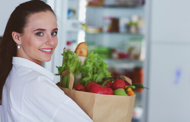 Young woman holding grocery shopping bag with vegetables .Standing in the kitchen. Woman in the kitchen looking at the camera