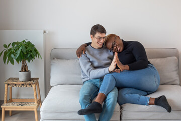 happy mixed couple sitting together on couch, hug