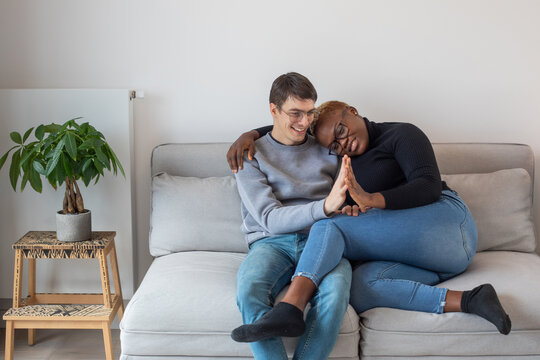 happy mixed couple sitting together on couch, hug - Powered by Adobe