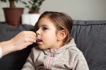 Caucasian girl portrait taking bronchitis treatment from dosage spoon at home