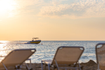 The backs of the sun loungers in front of the sea with a boat. Evening on the beach. Focus on the boat.