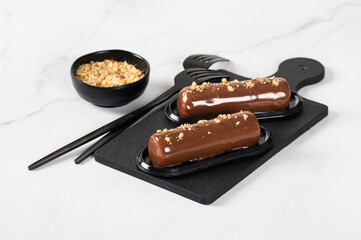 Chocolate walnut dessert in the form of a bar, with mirror glaze on a serving board on a light background