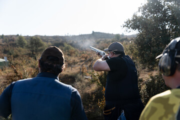 An adult man is shooting during a skeet shooting competition while two more participants are waiting behind © Miguel Serrano