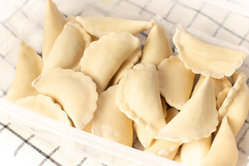 Frozen homemade dumplings in a plastic container on a white table