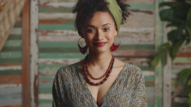 Young african american woman wearing ethno clothes with authentic accessories turning face to camera and smiling