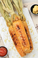 Grilled Sweet Corn with Butter and Shredded Mozarella. Served on White Plate