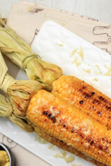 Grilled Sweet Corn with Butter and Shredded Mozarella. Served on White Plate