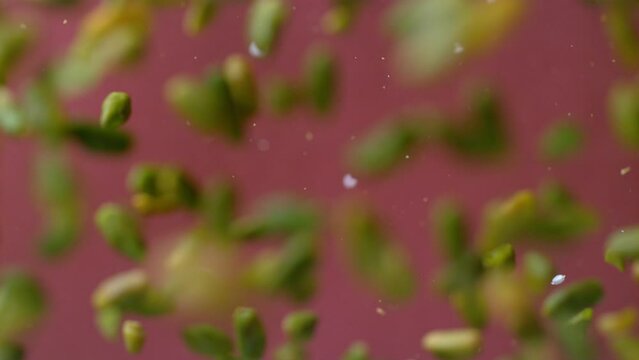 Close-up shot of salted peanuts flying towards the camera on a red background in slow motion. Green pistachios coming towards camera in 4K, Super slow motion