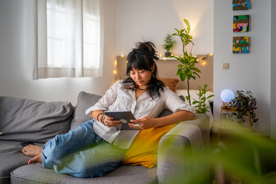 Asian Woman Checking The Tablet On The Couch At Home. 