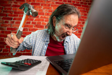 Funny portrait of angry crazy man attacking laptop with hammer while tax prep to balance budget getting debt deficit finding mistake in calculations.