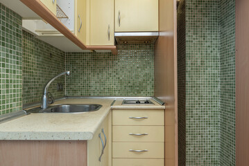 Small kitchen in a corner of a short-term rental apartment with green tiled walls