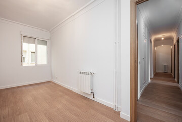 Empty room with plain walls, white aluminum radiator, window to interior patio and long corridor