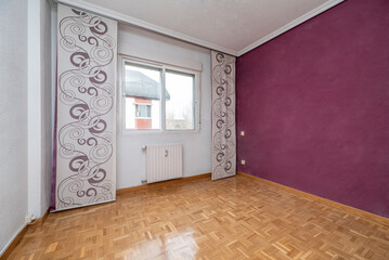 Empty room with plain white and purple painted walls with oak parquet flooring and patterned curtains
