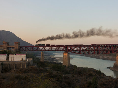 A steam train ( in silhouette )  reaching the castled  western departure gate of Attock bridge !