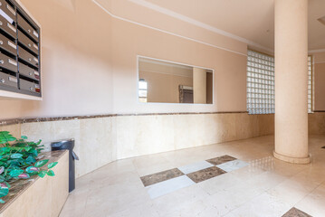 Entrance hall of a residential apartment building with walls tiled with cream-colored marble and a block wall