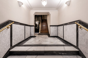 Entrance hall of a vintage apartment residential building with wooden staircase, white veined marble tiled half wall and elevator