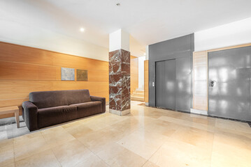 Entrance hall of a residential apartment building with marble floors and wood paneled walls and gray painted elevators