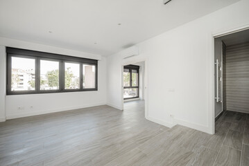 Empty room in a recently renovated apartment with large windows, an air conditioner and ceramic tile floors