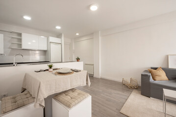 Naklejka na ściany i meble Furnished living room and kitchen with white cabinets in a vacation rental apartment with gray wooden floorboards