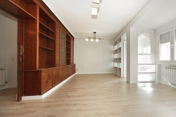 Living room with custom-made wooden bookcase made of mahogany wood, light wooden floors and built-in shelving next to the closed terrace