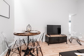 Eclectic living room with TV cabinet, methacrylate chairs and round wooden table and food service set