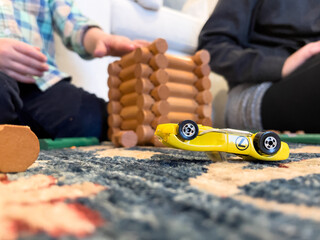 Low angle close-up of a child (non-recognizable) playing with Lincoln Logs and yellow, metal, toy car which is upside down on carpet